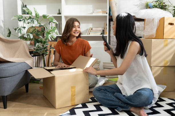 Hai người phụ nữ đang đóng gói thùng hàng tại nhà để gửi đồ cá nhân sang Đức bằng dịch vụ Door-to-Door, thể hiện sự tiện lợi và an toàn trong quá trình vận chuyển quốc tế.