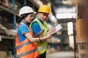 Nhân viên logistics đang kiểm tra hàng hóa trong kho, ghi chú chứng từ và đối chiếu đơn hàng – minh họa cho thủ tục xuất nhập khẩu khi gửi hàng đi Đức.