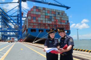 Cán bộ hải quan kiểm tra hồ sơ tại cảng biển với hệ thống container và tàu vận tải, minh họa quy trình giám sát trong xuất nhập khẩu tại chỗ 4 bên.